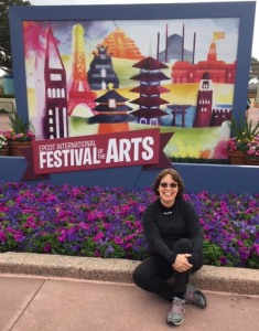 Linda Barnicott, Pittsburgh's Painter of Memories, poses in front of the Epcot International Festival of the Arts sign.