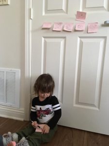 This photo features Aria Stadelman, Linda Barnicott's granddaughter, drawing while sitting on the floor. Some of her other drawings are taped to the wall behind her.