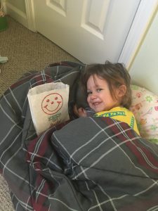 Aria Stadelman, granddaughter of Linda Barnicott, laying on the floor with an Eat 'n Park smiley cookie bag.