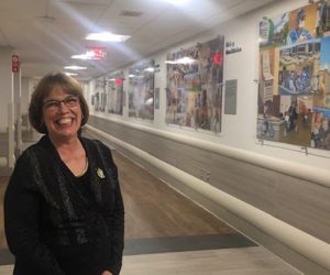 This image features Linda Barnicott posing in front of her new murals at Forbes Hospital