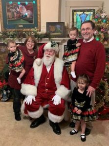 This image features Linda Barnicott, her husband, and granddaughters posing with Santa Claus.