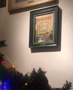 This image shows Linda Barnicott's original painting "Pickle Fun in Pittsburgh" hanging on the wall in her home.