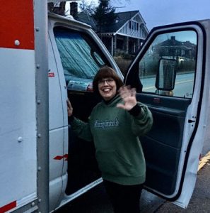 This image shows Linda Barnicott waving outside of a U-Haul truck.